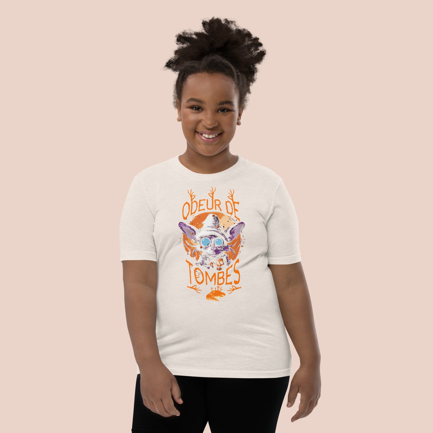 Fillet souriante portant un t-shirt d'Halloween pâle avec illustration d'un monstre et inscription Odeur de tombes. Vue du devant.
