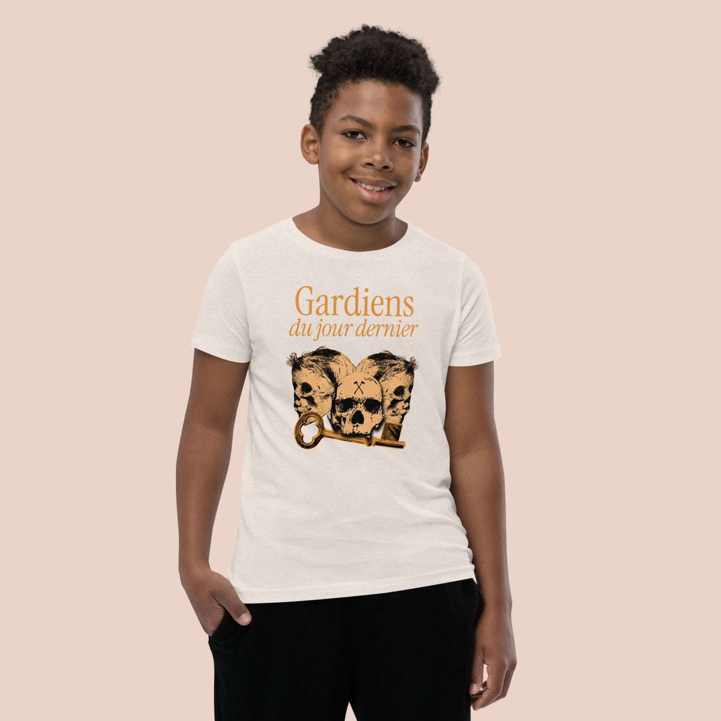 Garçon souriant portant un t-shirt de couleur naturel illustré de têtes de squelette et inscrit Gardiens du jour dernier. Vue du devant.
