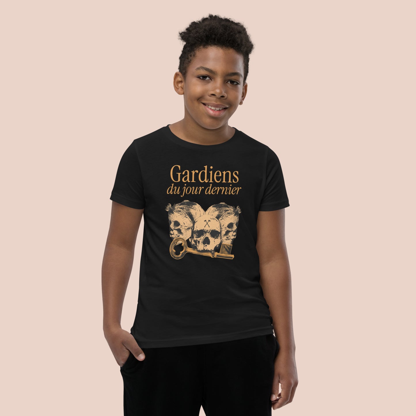 Garçon souriant portant un t-shirt noirl illustré de têtes de squelette et inscrit Gardiens du jour dernier. Vue du devant.