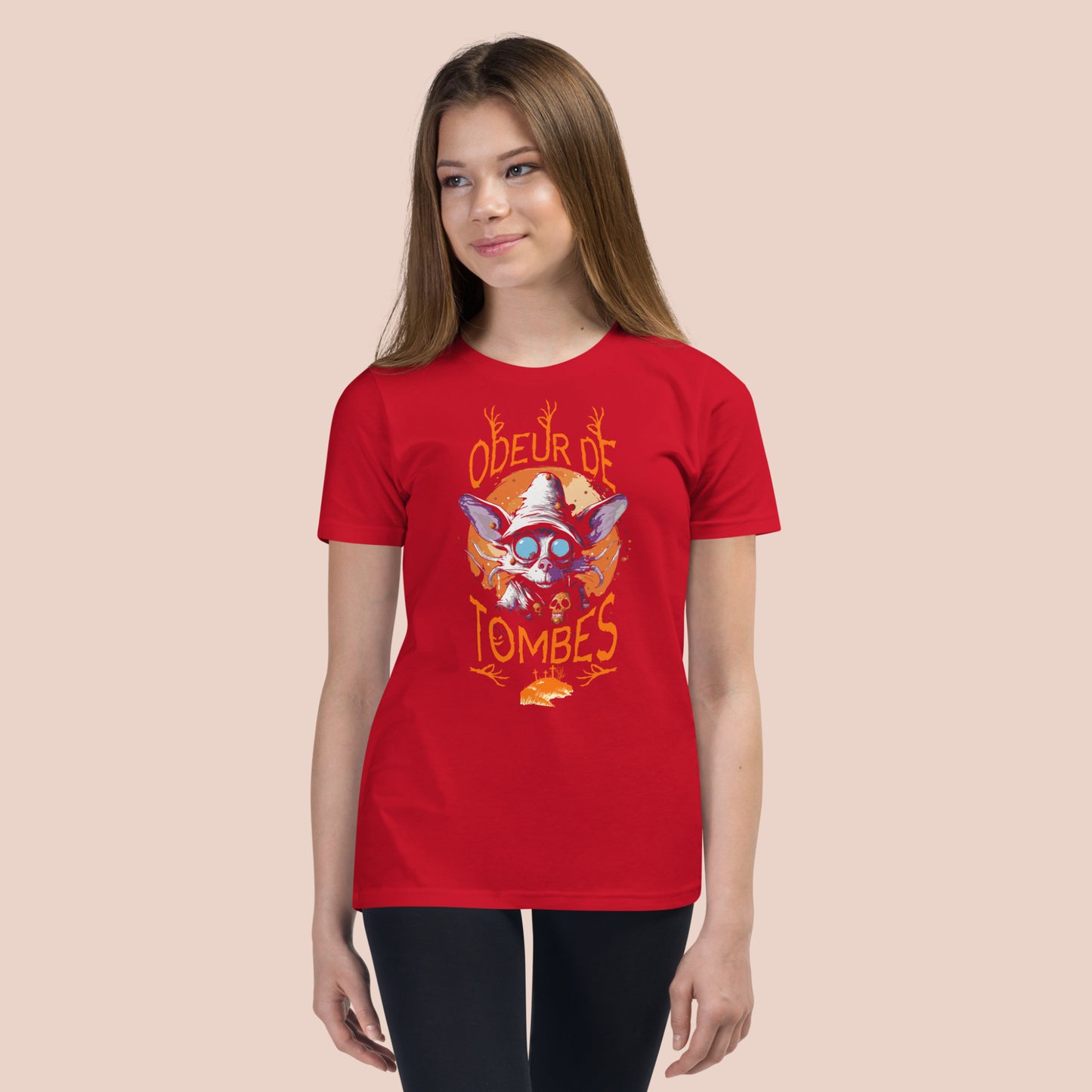 Jeune fille souriante portant un t-shirt rouge illustré d'un monstre et inscrit Odeur de tombes. Vue du devant.