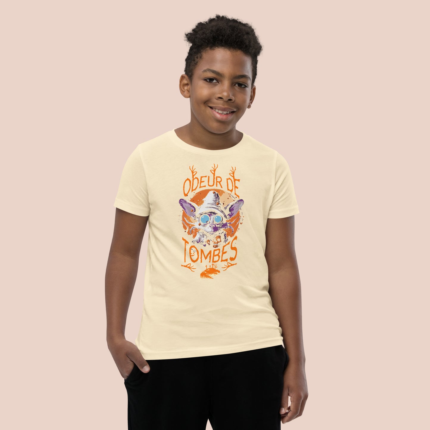 Garçcon souriant portant un t-shirt jaune pâle illustré d'un monstre et inscrit Odeur de tombes. Vue du devant.