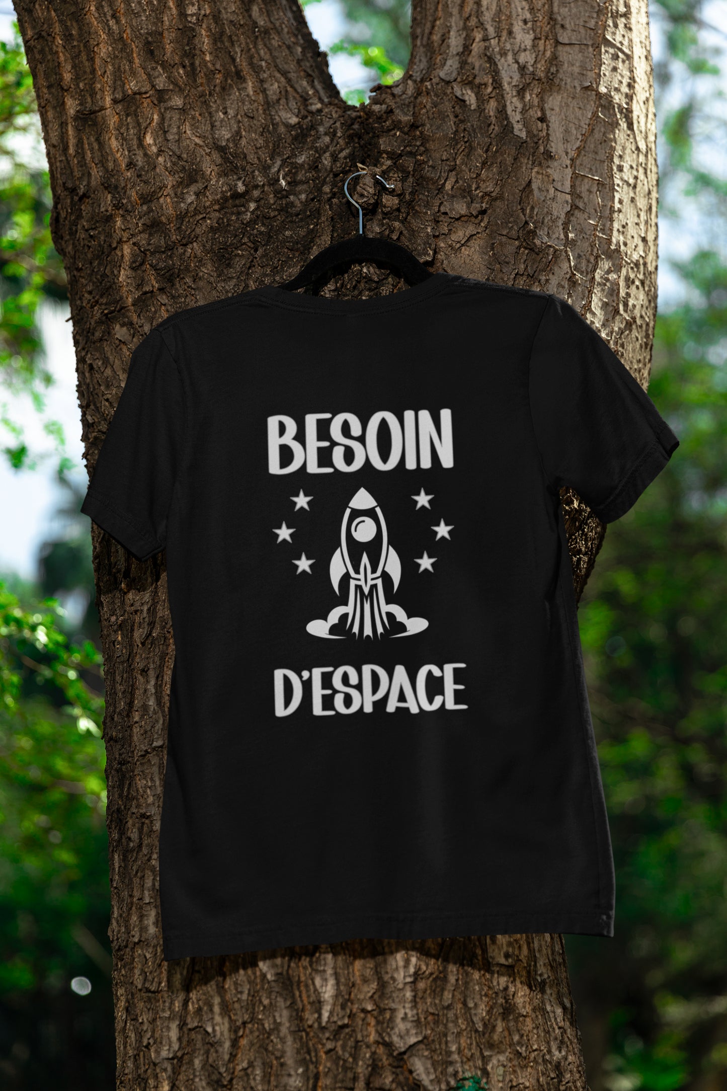 T-shirt noir sur cintre accroché sur un tronc d'arbre dans la nature. Imprimé Besoin d'espace. Vue du devant