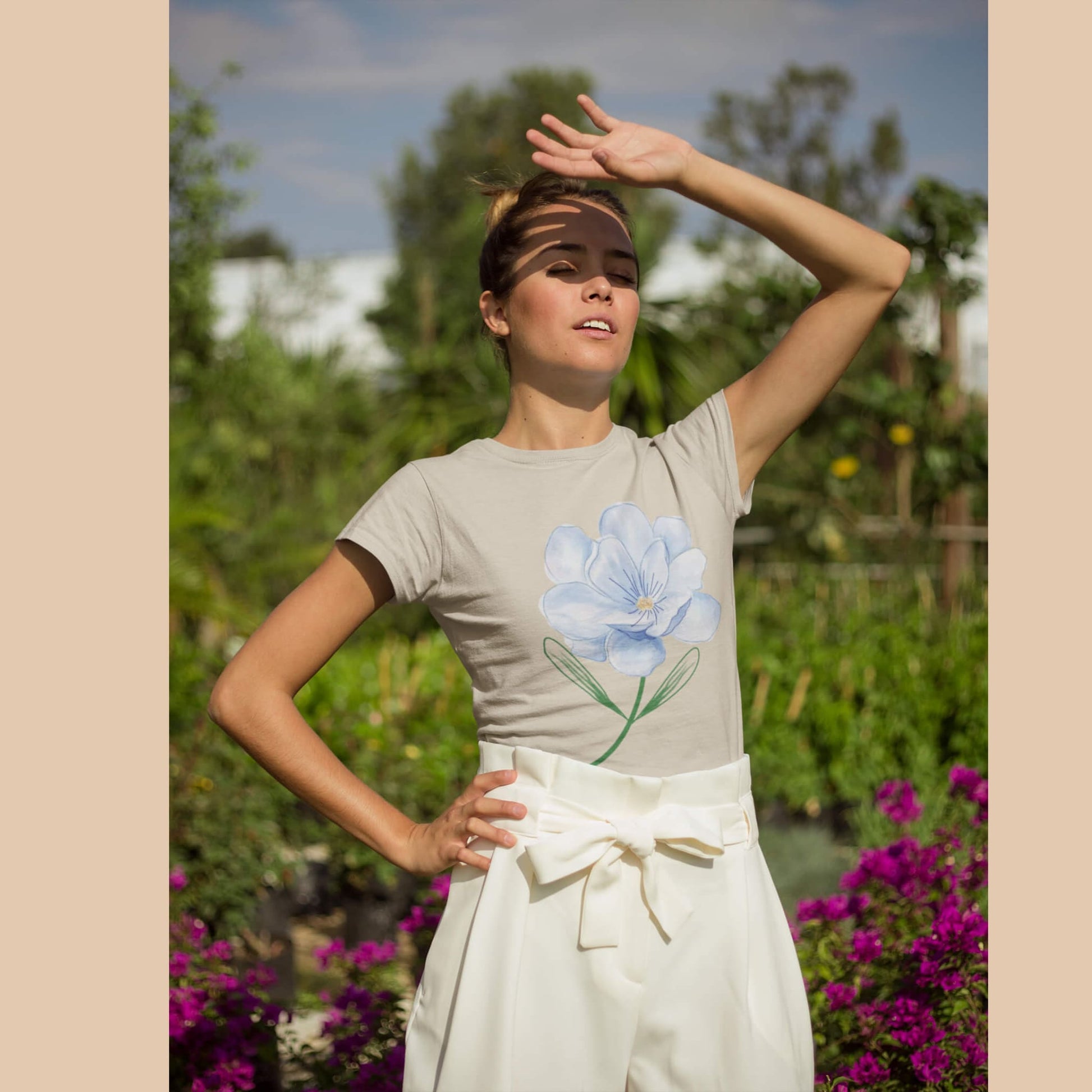 Femme portant un t-shirt beige en coton bio avec une fleur bleue à l’aquarelle, dans un jardin – Artic60