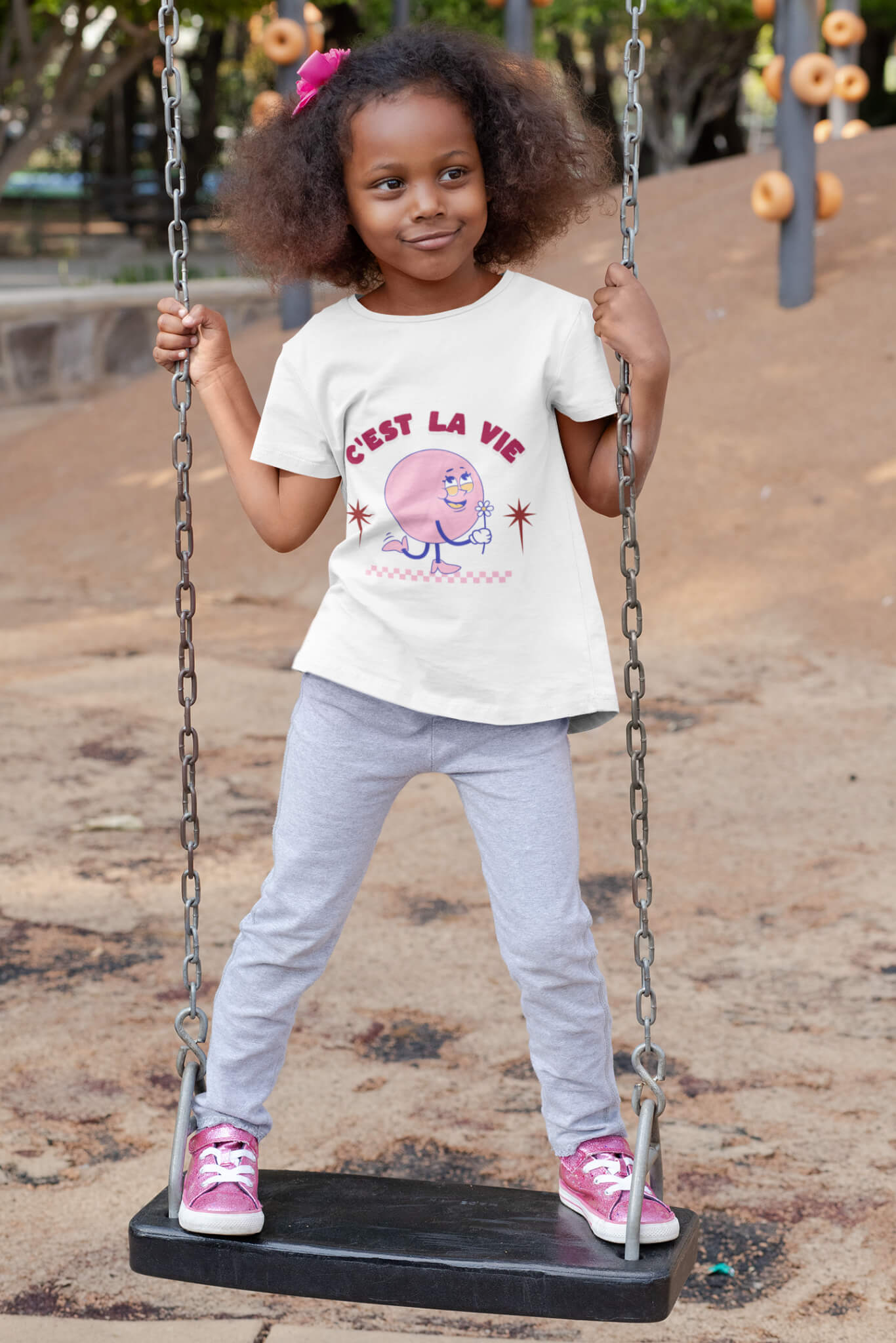 Fillette sur une balançoire portant un t-shirt blanc avec le design « C’est la vie » en style rétro – Artic60