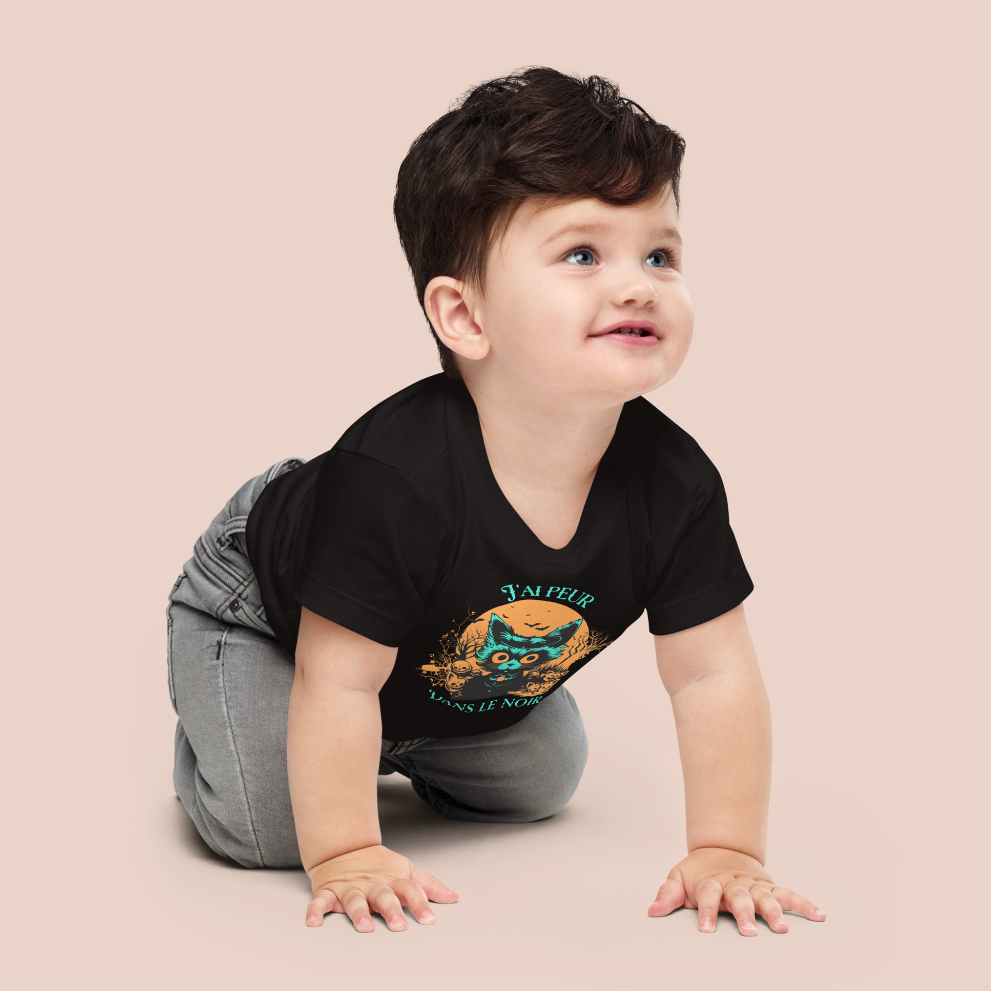 Bébé à quatre pattes au cheveux noirs portant un t-shirt d'Halloween noir avec une illustration d'un chat effrayé et l'inscription J'ai peur dans le noir. Vue du devant.