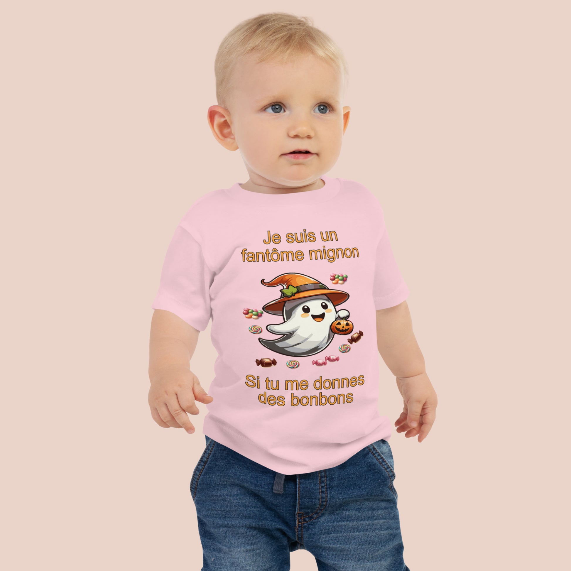 bébé portant un t-shirt d'Halloween rose imprimé d'un mignon fantôme entouré de bonbons et inscrit Je suis un fantôme mignon si tu me donnes des bonbons. Vue du devant.