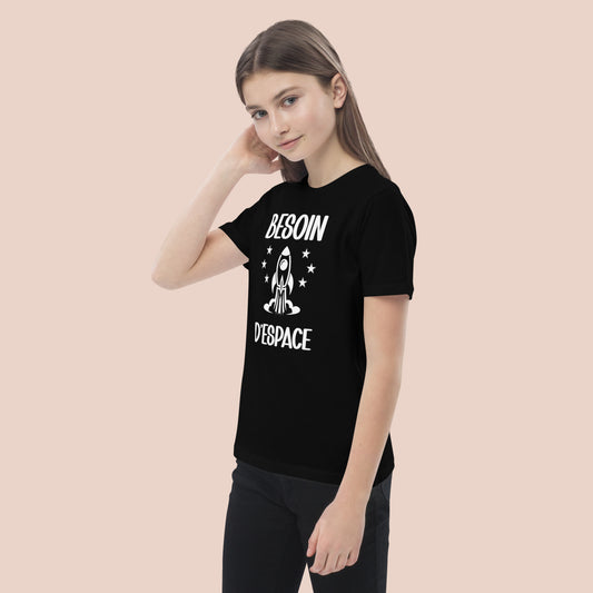 Jeune fille souriante, main dans les cheveux, portant un T-shirt noir fait de conton biologique.Impression du texte : Besoin d'espace. Vue du demi-devant gauche