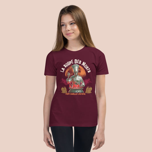 Fille souriante portant un t-shirt marron 
avec illustration d'un chef monstre-squelette et insciption La soupe des morts. Vue du devant.