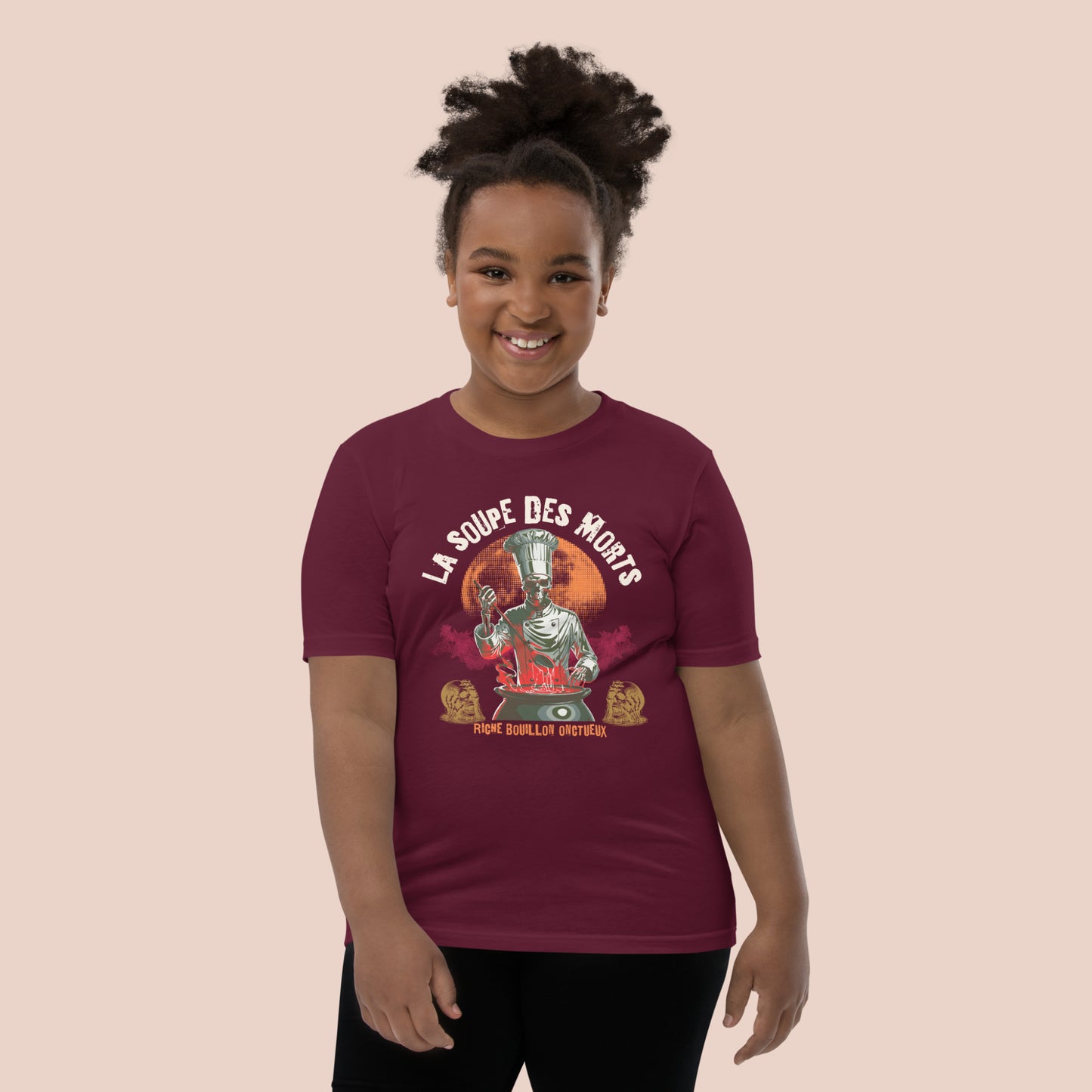 Fillet joyeuse portant un t-shirt d'Halloween marron avec illustration d'un chef squelette-monstre et inscription La soupe des morts. Vue du devant.