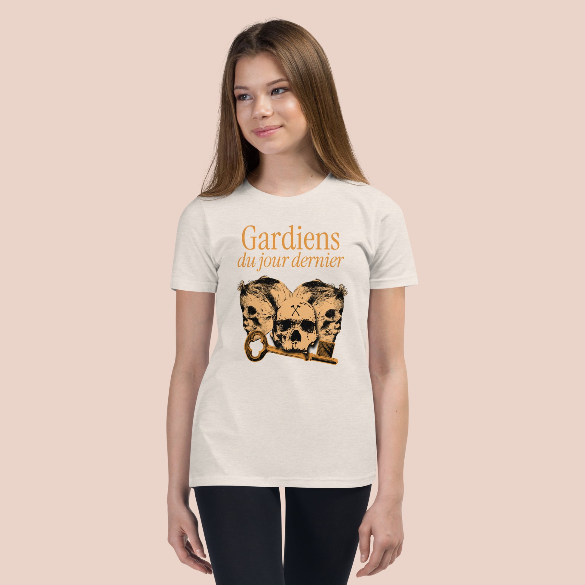 Fille souriante portant un t-shirt de couleur naturel illustré de têtes de squelette et inscrit Gardiens du jour dernier. Vue du devant.