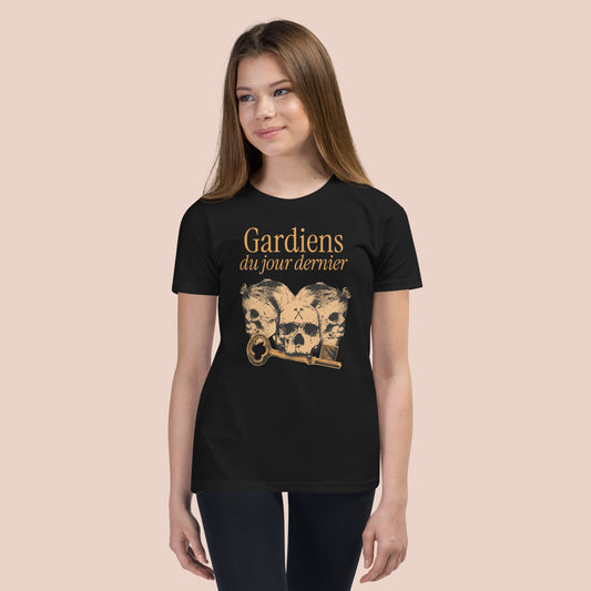 Fille souriante portant un t-shirt noir 
illustré de têtes de squelette et inscrit Gardiens du jour dernier. Vue du devant.
